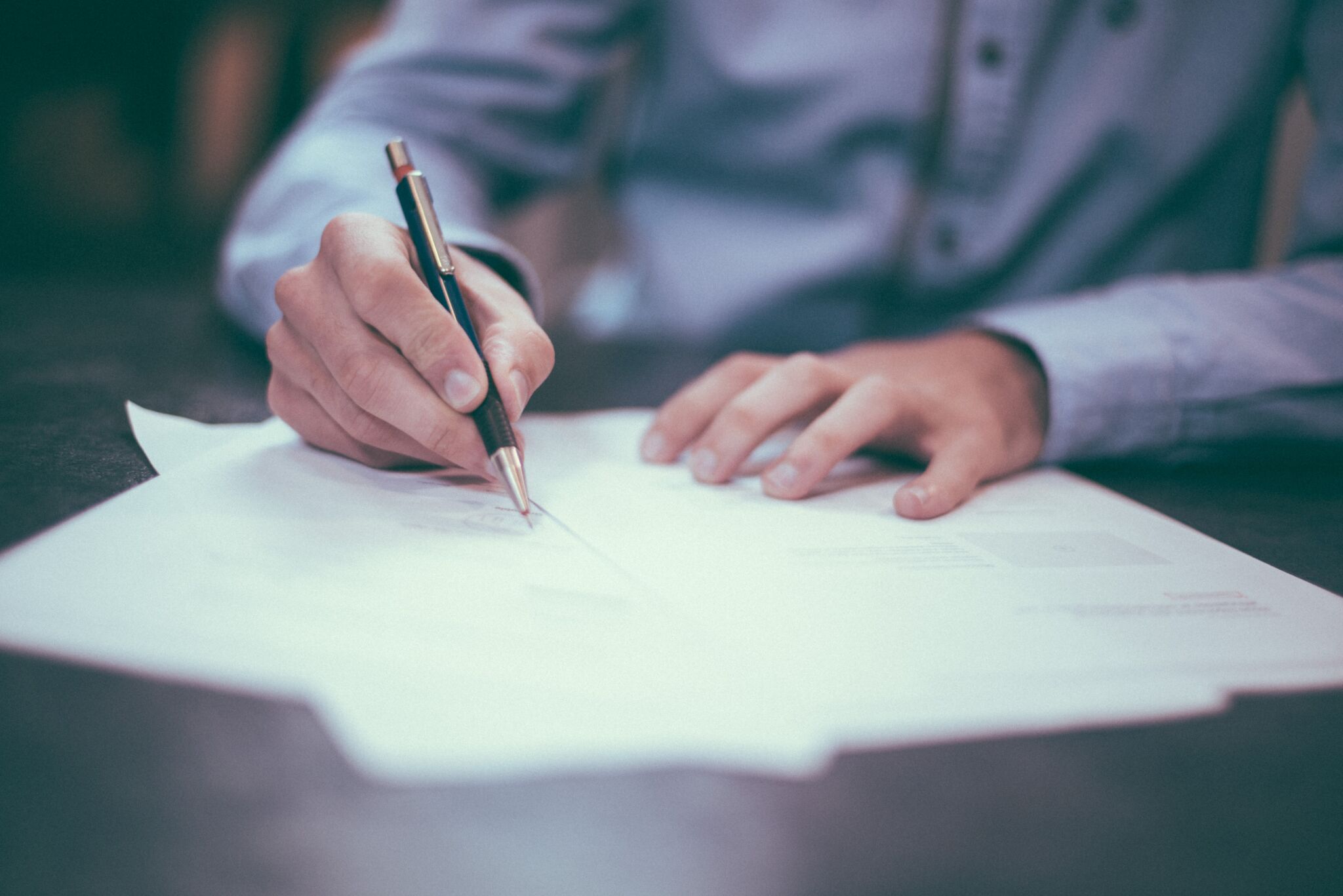 photo of man signing a paper on a desk/table